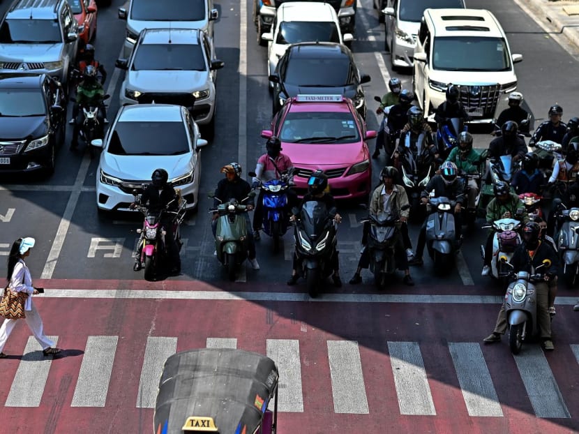 Motorcyclists wait under the shade as a woman crosses a traffic intersection in Bangkok on April 25, 2024. 